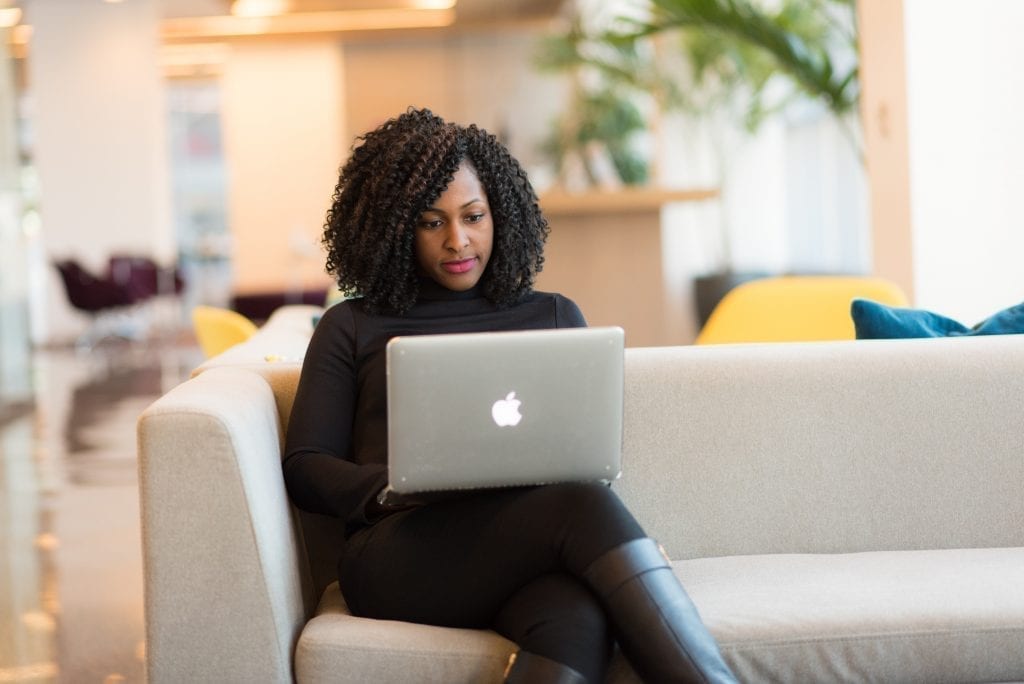 Quantos projetos colocar no portfolio: imagem de mulher com um laptop no colo, sentada em um sofá.